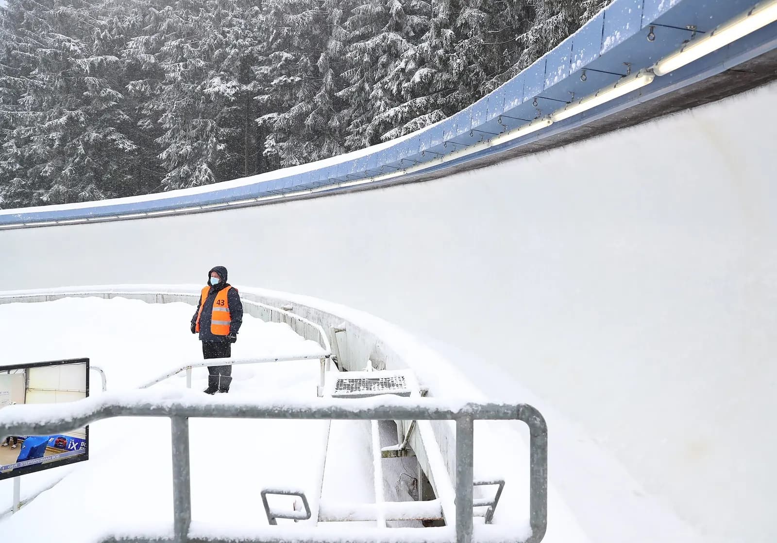 Steile, vereiste Kurvenwand des Eiskanals mit einem Streckenposten in Warnweste