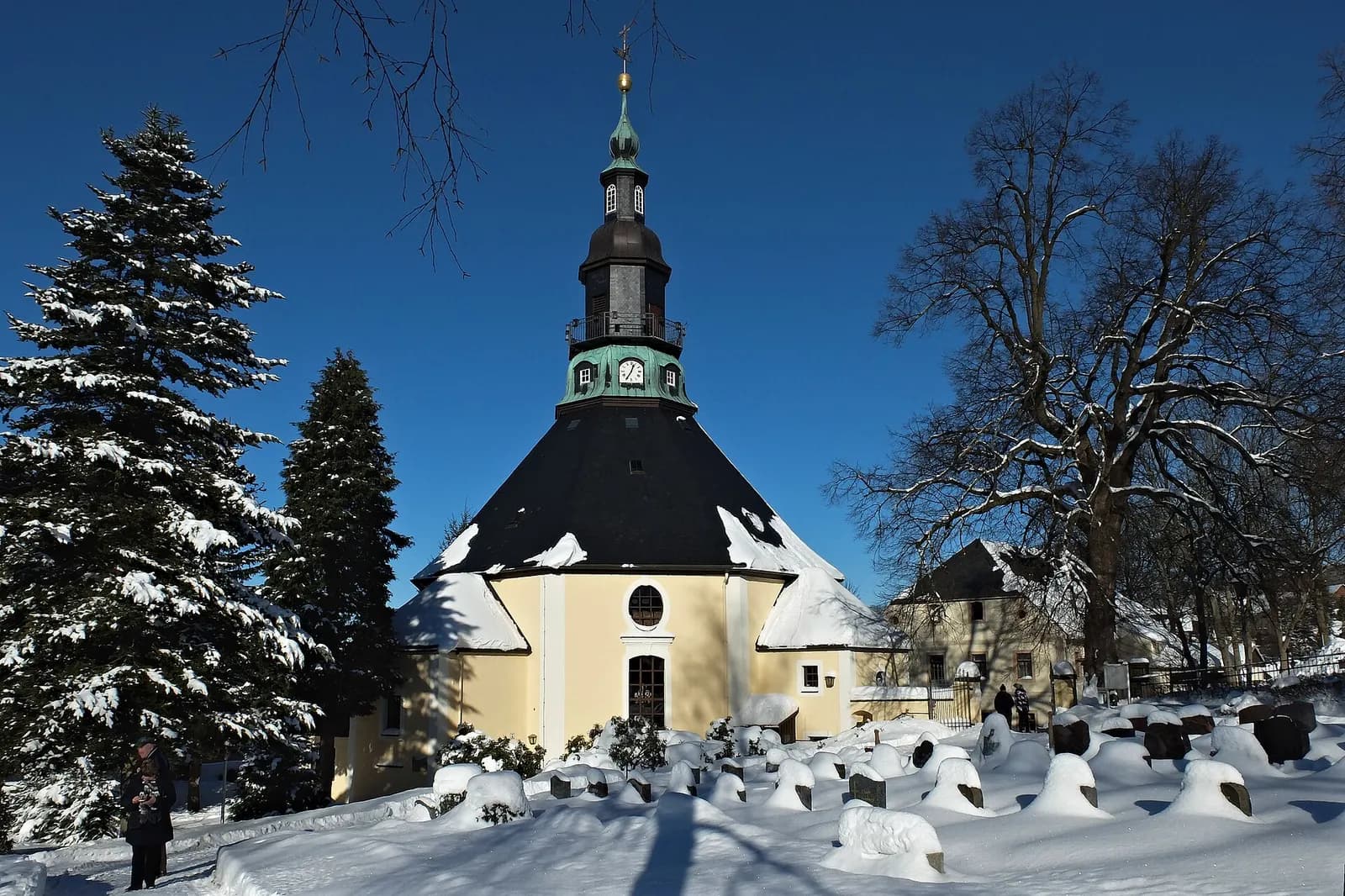 Die achteckige Bergkirche Seiffen mit grünem Turm im verschneiten Kirchhof unter blauem Himmel